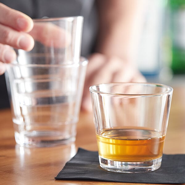 A person pouring a shot of whiskey into an Acopa Select stackable rocks glass on a table.