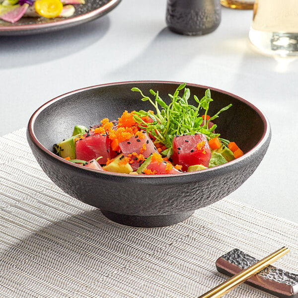 A black matte textured Acopa Heika stoneware bowl filled with sushi on a table.