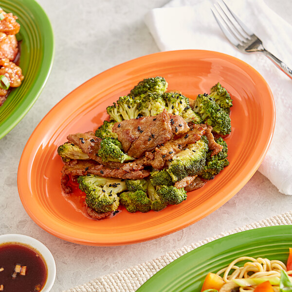 A plate of food with broccoli, black sesame seeds, and other dishes on an Acopa Valencia Orange oval stoneware coupe platter.