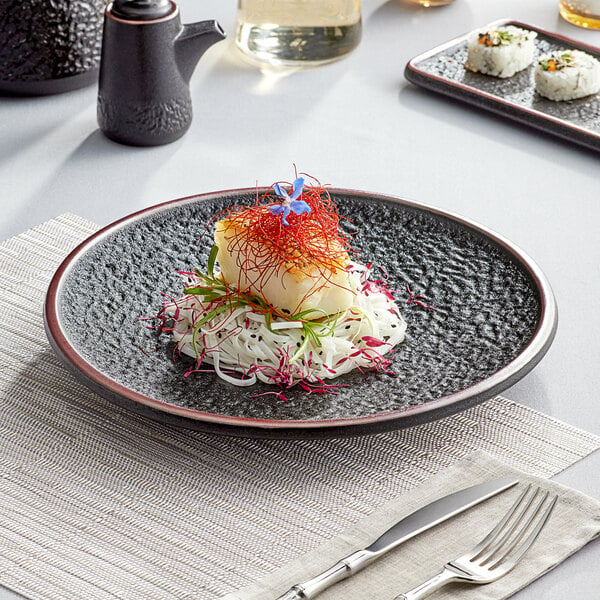 A black Acopa Heika stoneware plate with food on it and a fork and knife on a napkin.