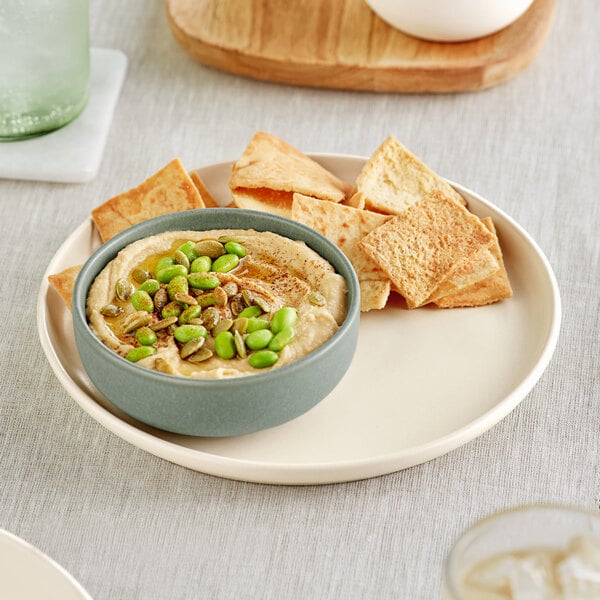 A plate with a triangular piece of hummus and crackers.