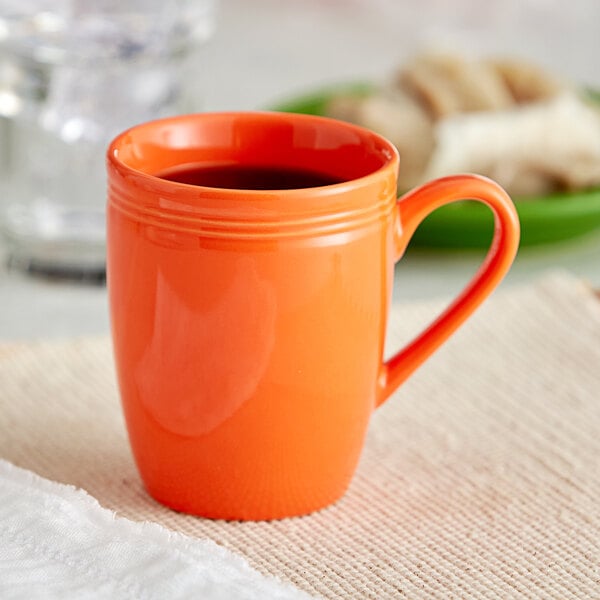 An orange Acopa Capri stoneware mug with a handle on a table with a green plate of food.