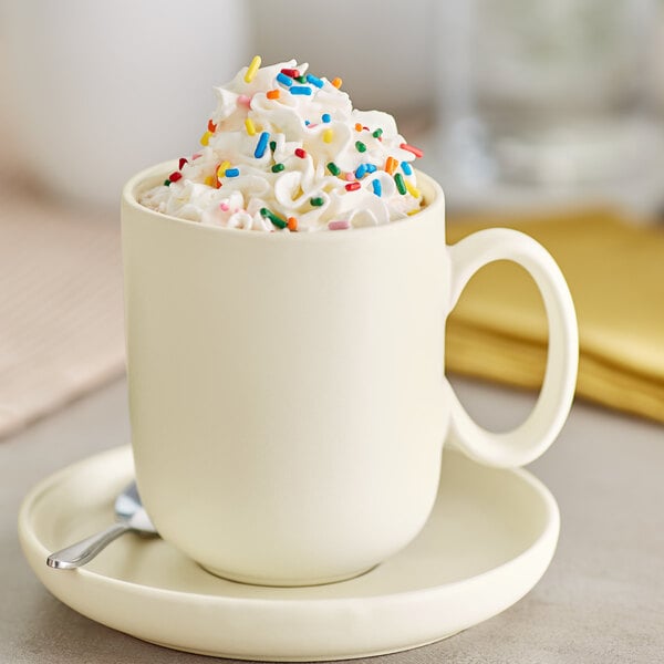 A fog white Acopa Pangea porcelain mug filled with coffee and sprinkles with a spoon.