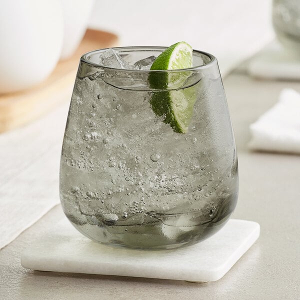 An Acopa Pangea stemless wine glass with ice and a lime wedge on a coaster.