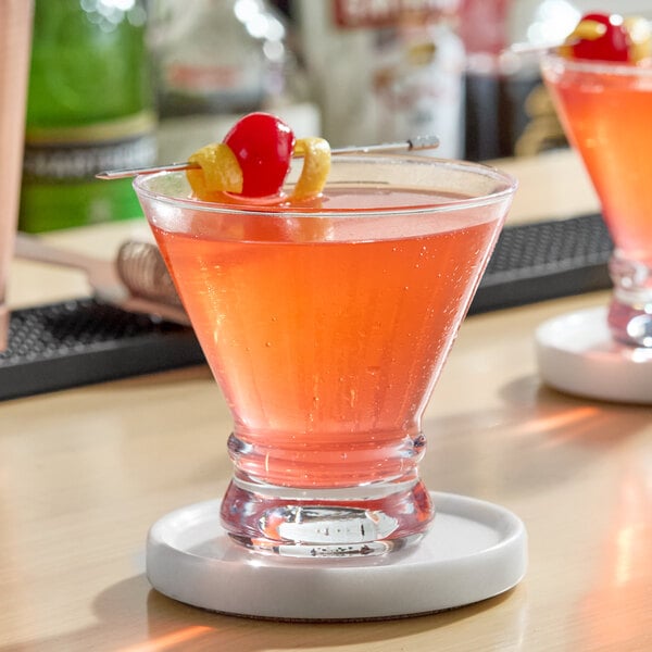 A stemless martini glass filled with a pink cocktail and garnished with a cherry and lemon twist on a pick.