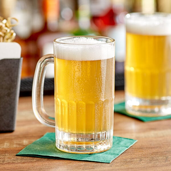 Two Acopa beer mugs filled with beer on a table.