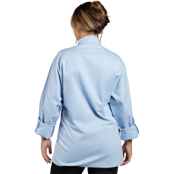 A woman wearing a sky blue Uncommon Chef Orleans long sleeve chef coat.