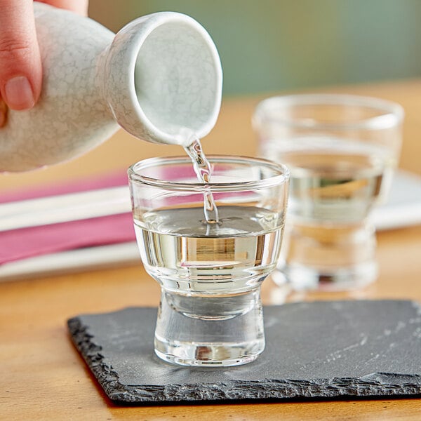 A person pouring cold sake into an Acopa Select 2 oz. sake glass.