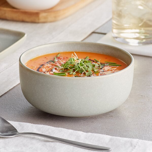 A bowl of soup with sprouts on top in an Acopa Pangea ash matte porcelain bowl with a spoon.