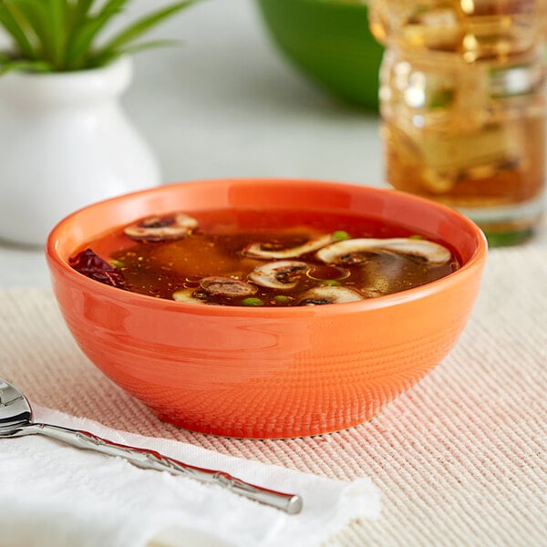 A close-up of a green Acopa Capri Valencia Orange stoneware bistro bowl filled with soup with mushrooms and onions.