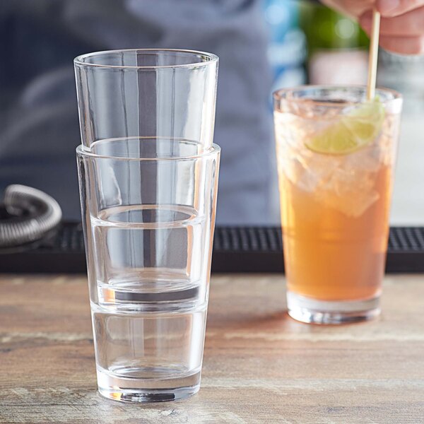 A person holding an Acopa Select 12 oz. highball glass filled with a drink, ice, and a lime wedge.