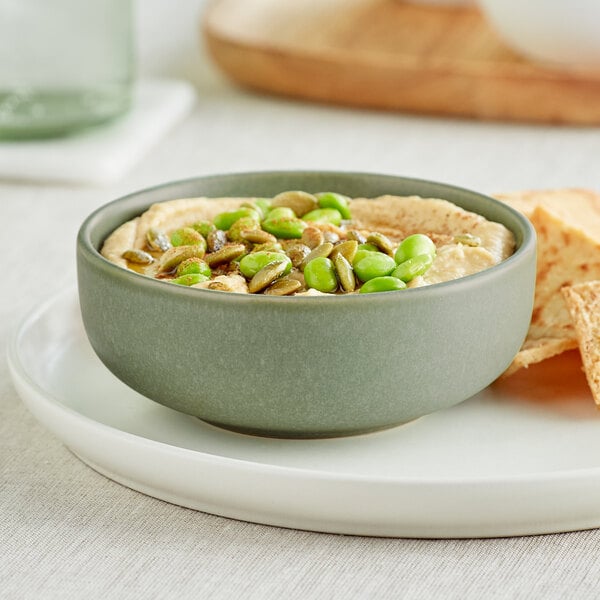 An Acopa Pangea sage matte porcelain nappie bowl filled with hummus on a plate.