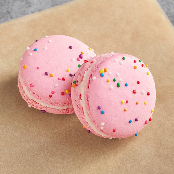 Two pink macarons with sprinkles on a brown paper.