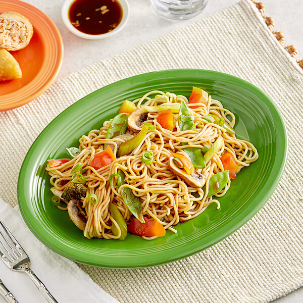 An Acopa Capri palm green oval stoneware coupe platter with noodles and vegetables on it.