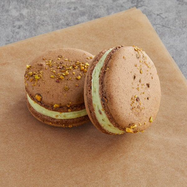 Two Macaron Centrale macarons with green and yellow filling on a table.