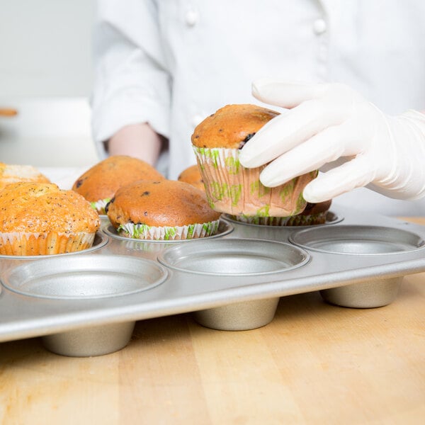 A person wearing white gloves placing a muffin in a Chicago Metallic jumbo muffin tin.