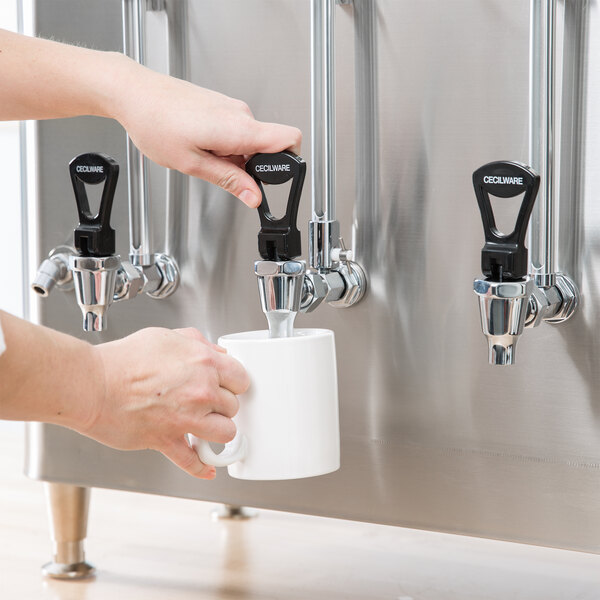 A person using a Cecilware automatic coffee urn to fill a white mug with coffee.