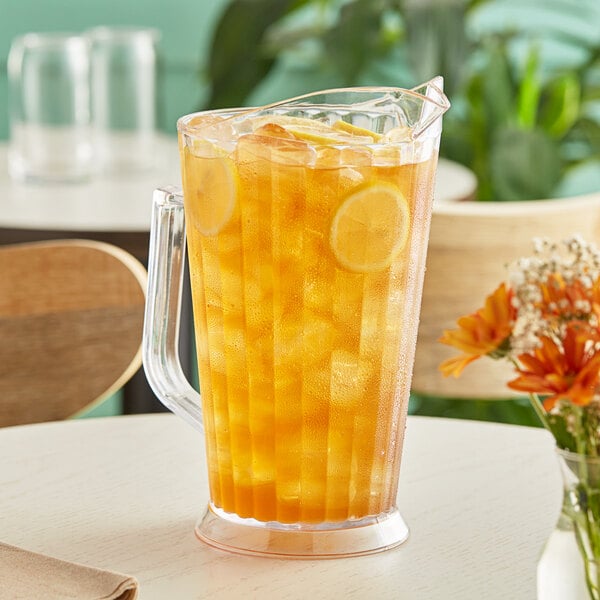 A Choice polycarbonate beverage pitcher of ice tea with lemons and flowers.