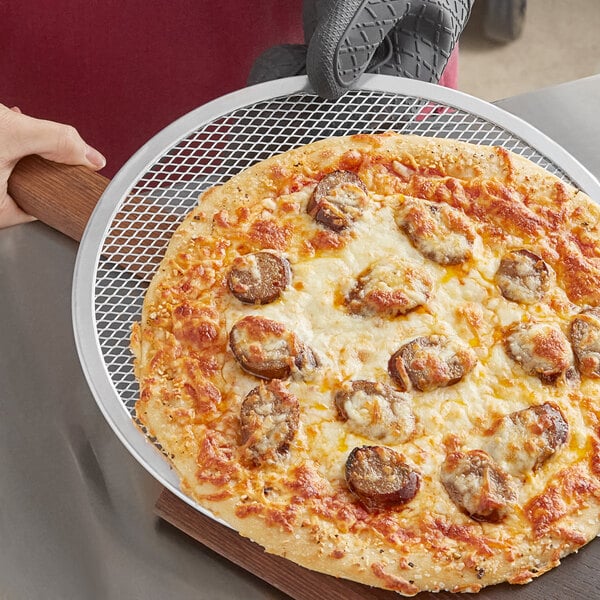 A hand holding a pizza on an aluminum pizza screen.