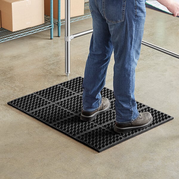 A person standing on a Choice black anti-fatigue floor mat.