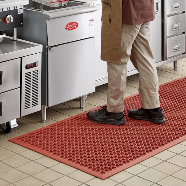 A man standing on a red Lavex Heavy-Duty Rubber Anti-Fatigue floor mat in a kitchen.