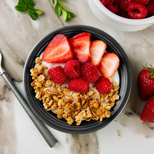 A Tuxton Concentrix black china bowl filled with granola, strawberries, and raspberries.