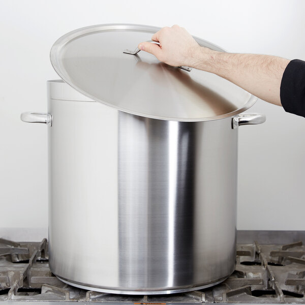 A person holding a Vollrath Centurion stainless steel stock pot lid over a large silver pot.