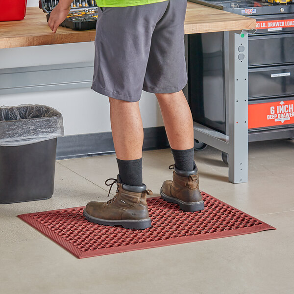 A person standing on a Choice red rubber anti-fatigue floor mat.