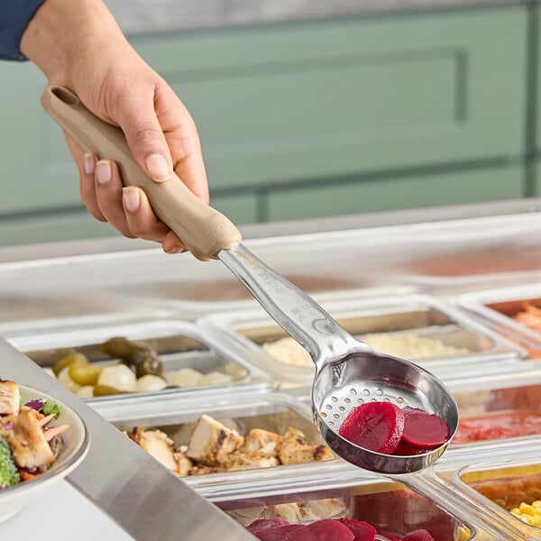 A person using a Vollrath Ivory Perforated Round Spoodle over a bowl of food.