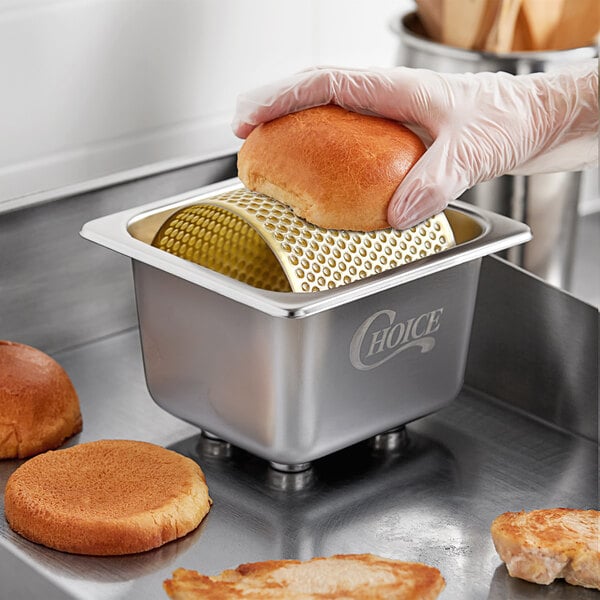A person using a Choice stainless steel butter spreader to cut a brown bun.