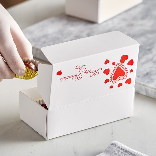 A hand holding a chocolate candy in a Valentine's Day candy box.