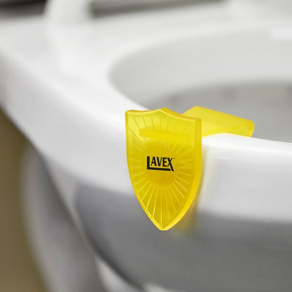 A yellow plastic clip with a shield shape on a toilet bowl.