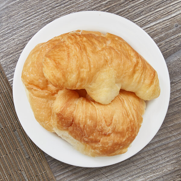 An Arcoroc white porcelain B&B plate with croissants on a wood surface.