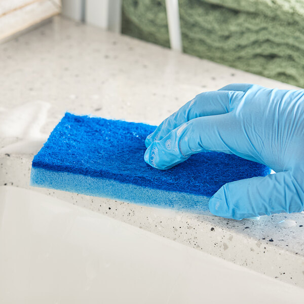 A gloved hand using a Lavex blue sponge to clean a counter.