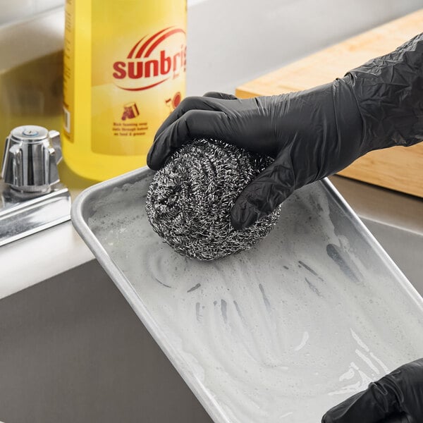A stainless steel scrubber being used to clean a metal tray.