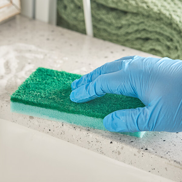 A gloved hand using a Lavex green sponge to clean a counter.
