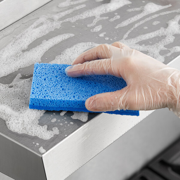 A hand in a glove using a Lavex blue sponge to clean a stainless steel sink.