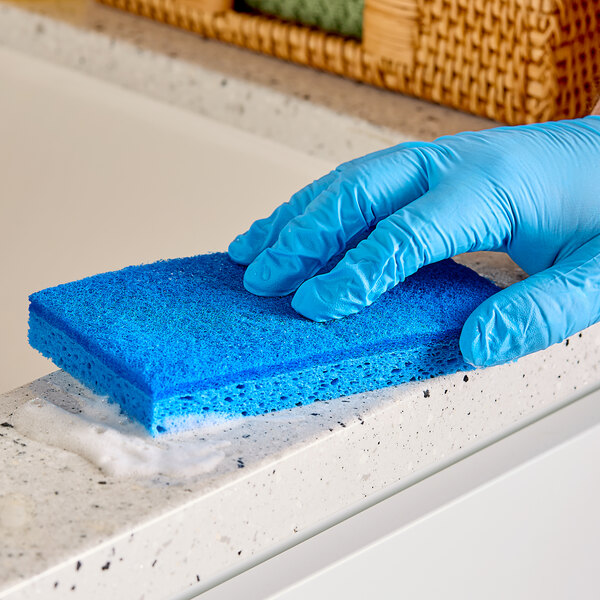 A hand in a blue glove using a Lavex blue sponge to clean a counter.