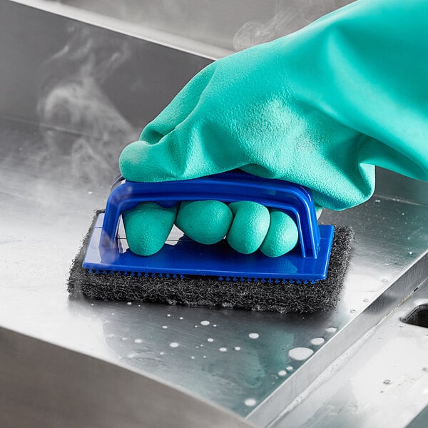 A hand in a green glove using a blue Choice sponge to clean a metal surface.