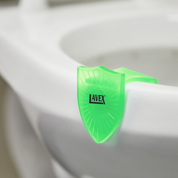 A green plastic Lavex Apple Scent Gel toilet bowl clip on a toilet.