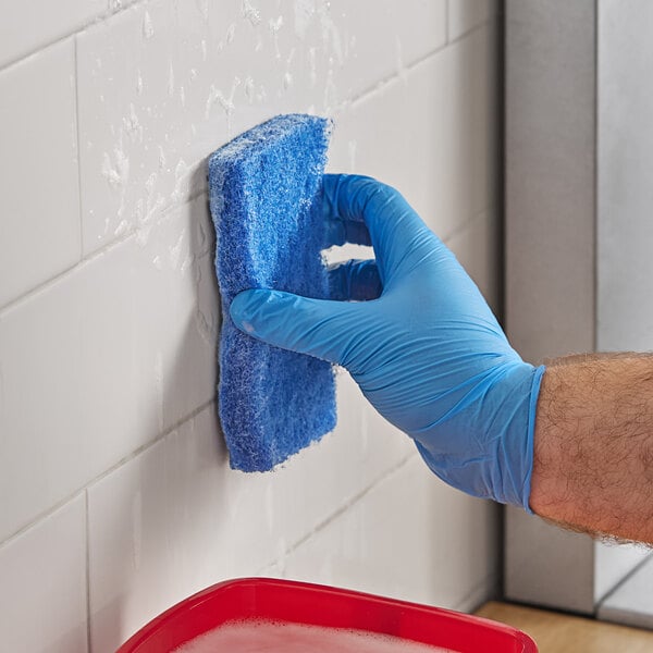 A person in a blue glove using a Lavex medium-duty blue scouring pad to clean a wall.