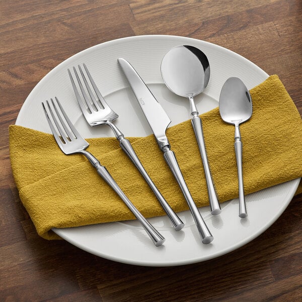 An Acopa Hepburn stainless steel flatware set on a yellow napkin with a knife and spoon.