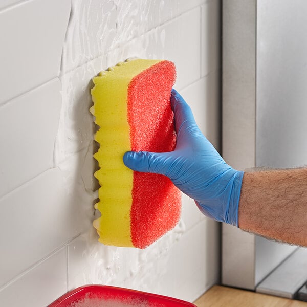 A gloved hand using a Lavex jumbo double-action sponge to clean a wall.