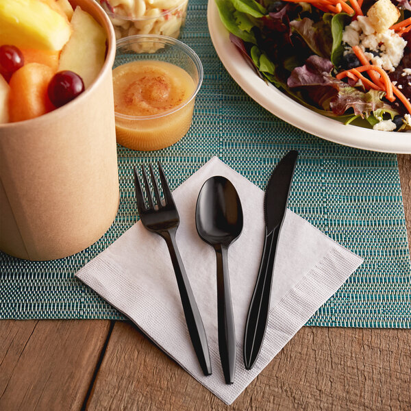 A table with a bowl of fruit, a bowl of salad, and black plastic utensils, including a medium weight black plastic knife.