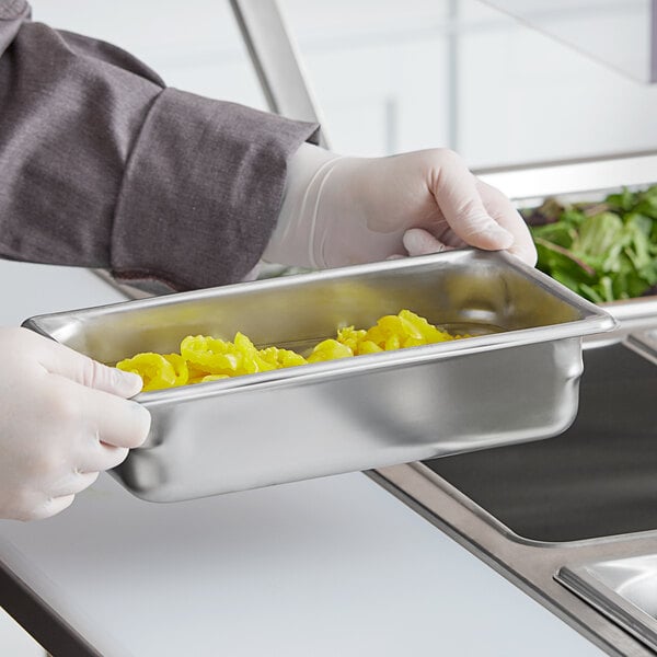 A person holding a Vollrath stainless steel pan with food in it.