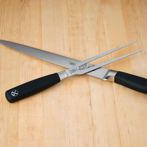 A Mercer Culinary Genesis Forged Carving Fork and Knife on a wooden surface.