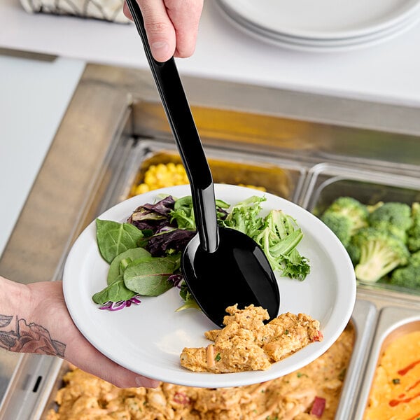 A person holding a plate of salad with a black Carlisle salad bar spoon.