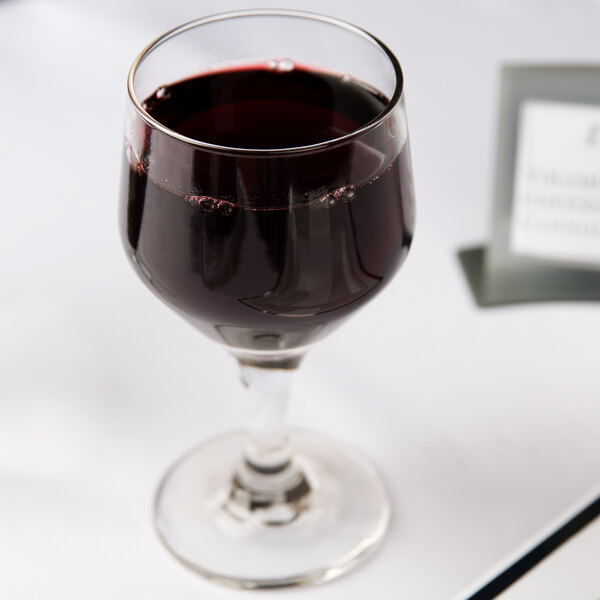 A Libbey wine glass filled with red wine on a table.