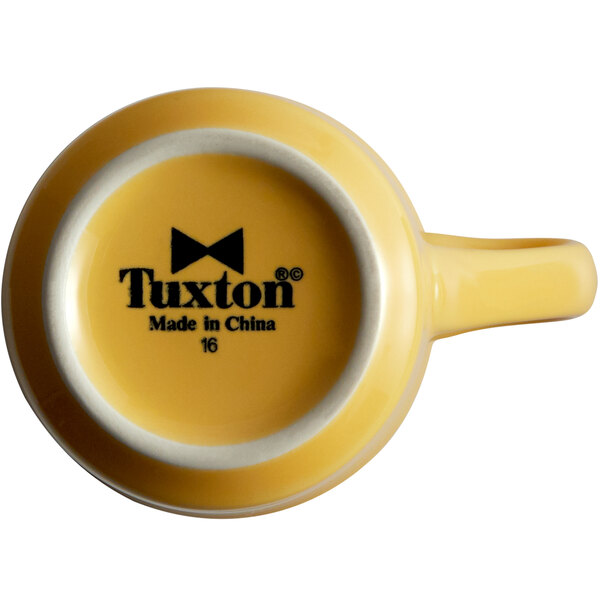 A yellow Tuxton Concentrix mug with black text on the side.