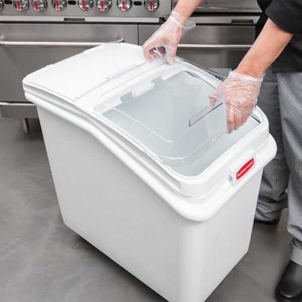 A person wearing gloves opens a white plastic container with a Rubbermaid sliding lid.